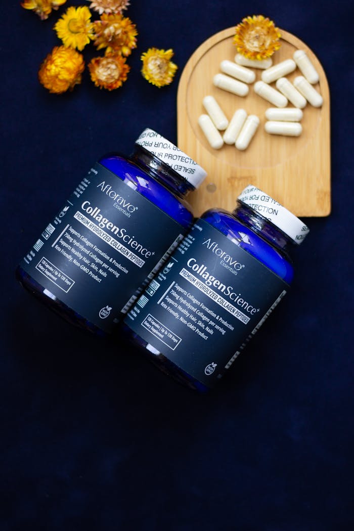 Two bottles of collagen supplements with capsules and flowers on a dark background.